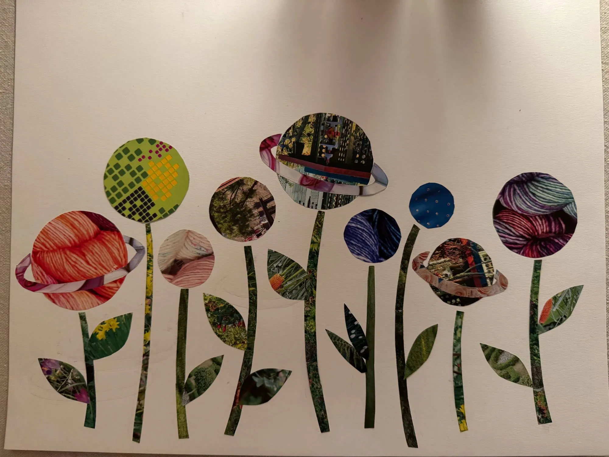 A collage of various patterns cut out in the shape of planets (some with rings, some without) on top of stems with leaves