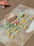 A bunch of unfired small clay carrots and apples, along with a basket, a cabbage, and a frog