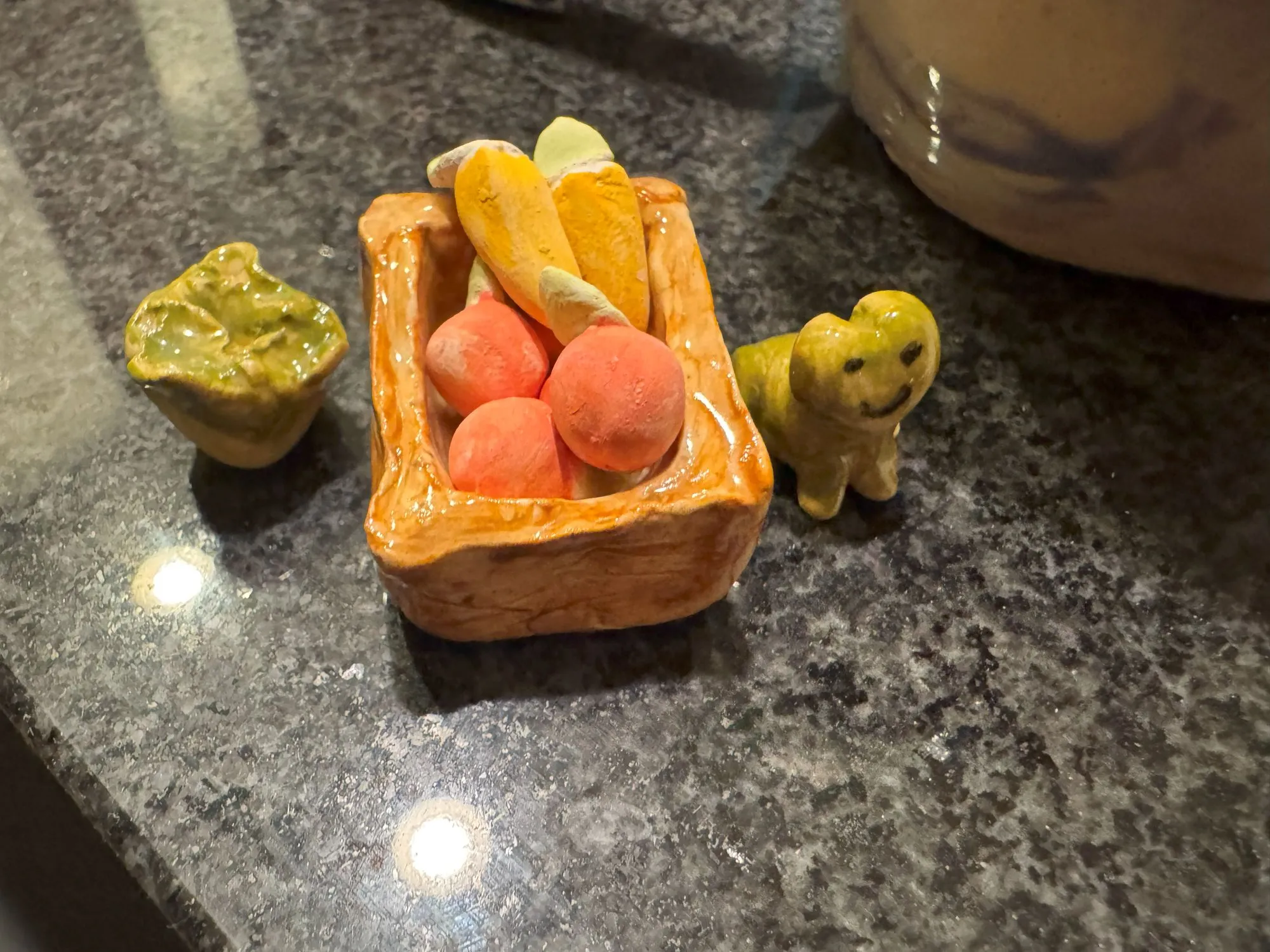 A collection of fired clay pieces, including a basket, carrots, apples, a cabbage, and a frog