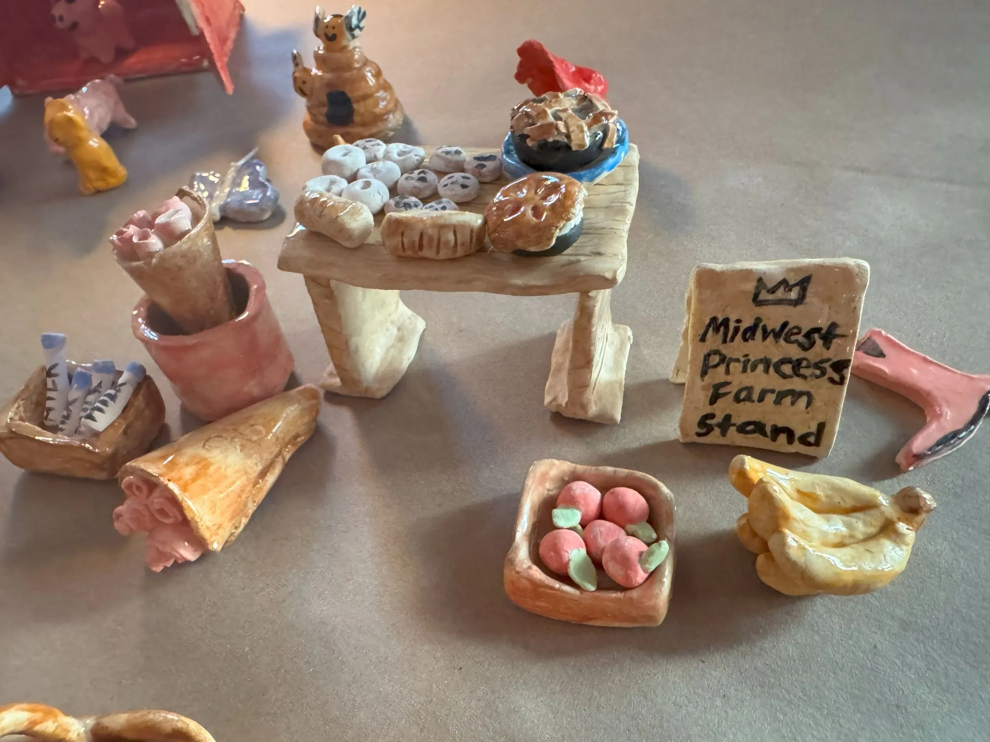 A ceramic farm stand with various baked goods, flowers, and fruit