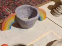 An unfired purple plant pot with rainbow arms coming from either side