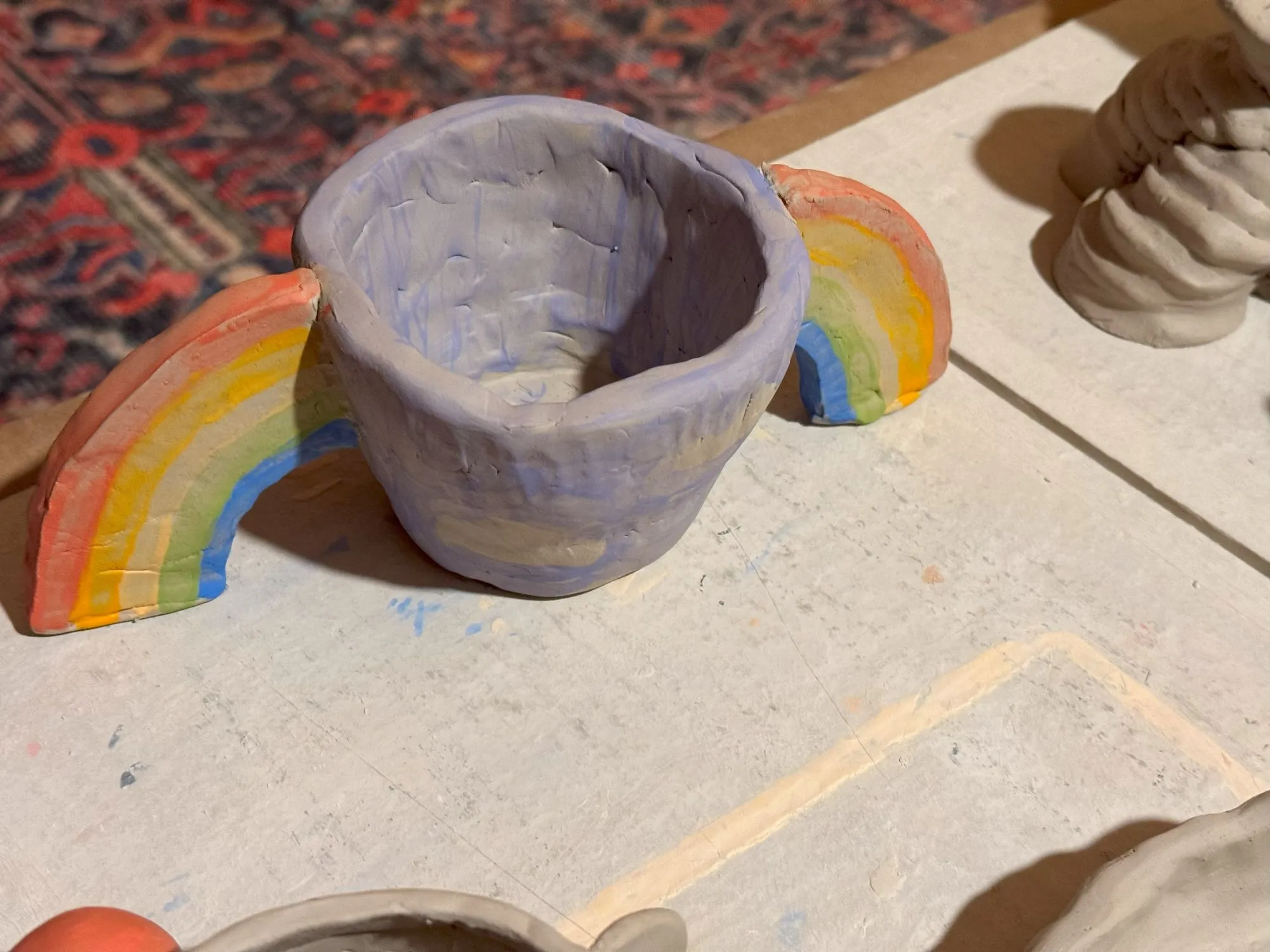 An unfired purple plant pot with rainbow arms coming from either side