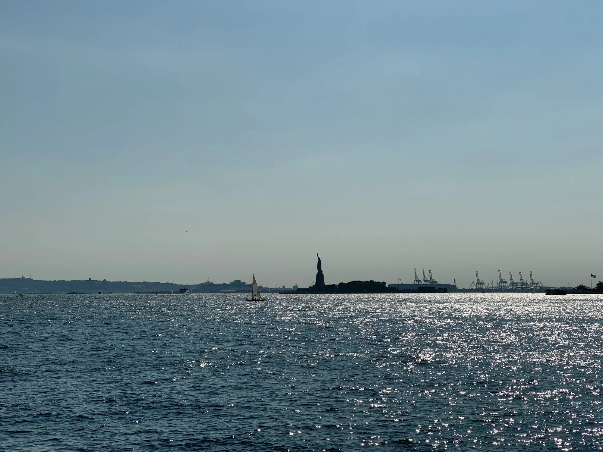 A picture of water with a silhouette of the Statue of Liberty visible in the distance