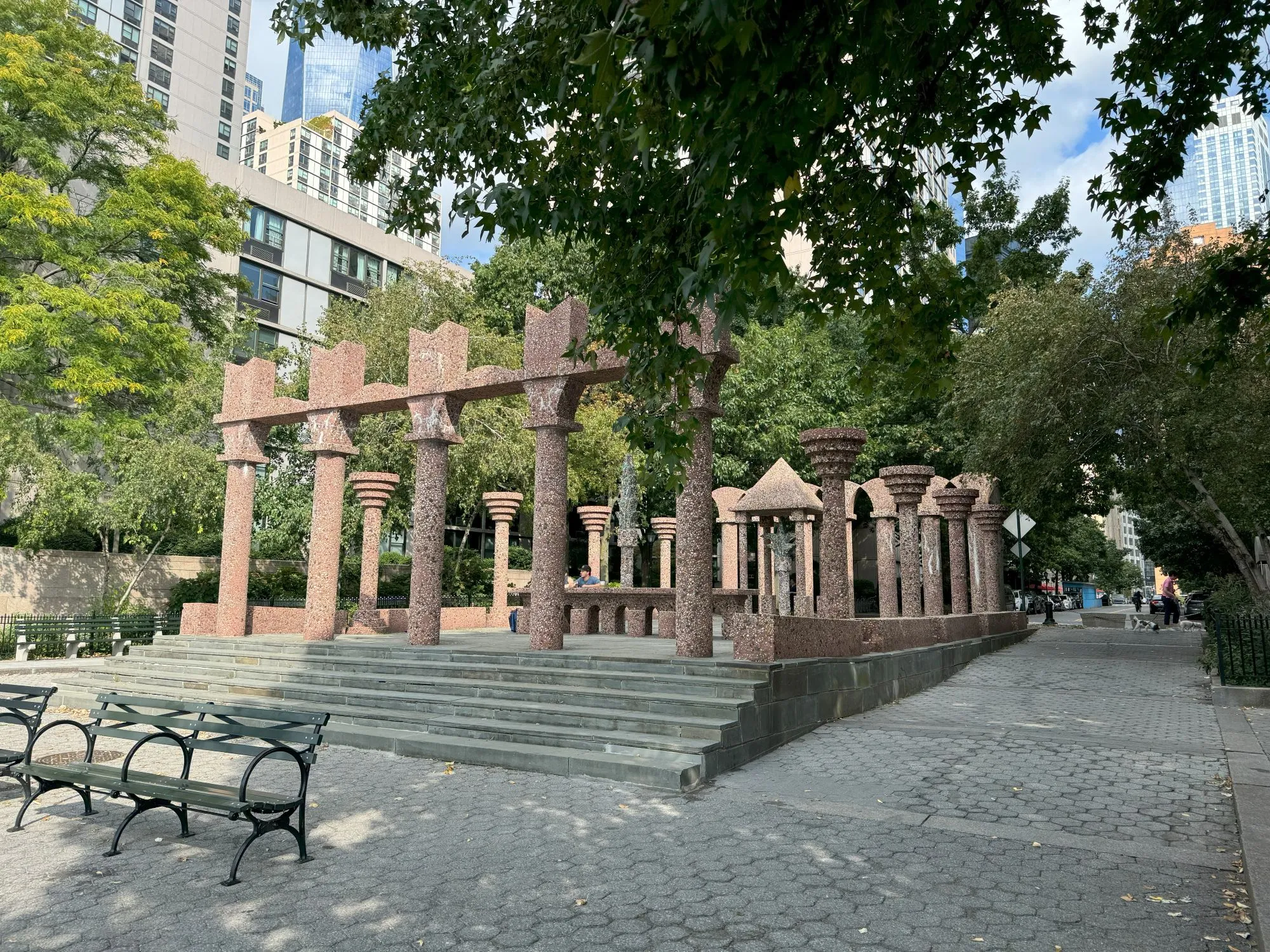 A structure with many columns in a pedestrian area surrounded by trees