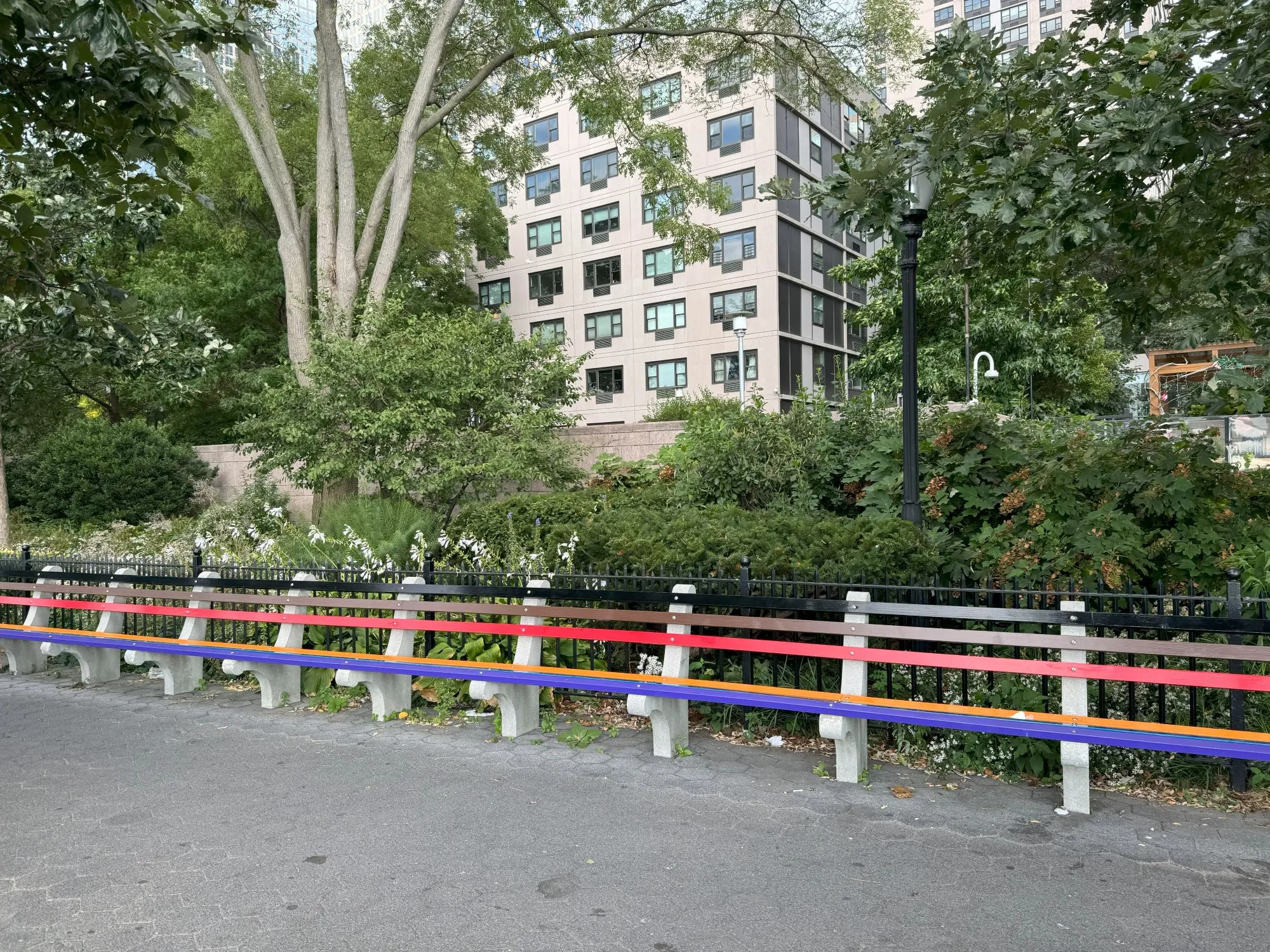 A long bench with the panels painted multiple colors on the side of a pedestrian area