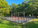 A swingset in a fenced playground surrounded by green trees