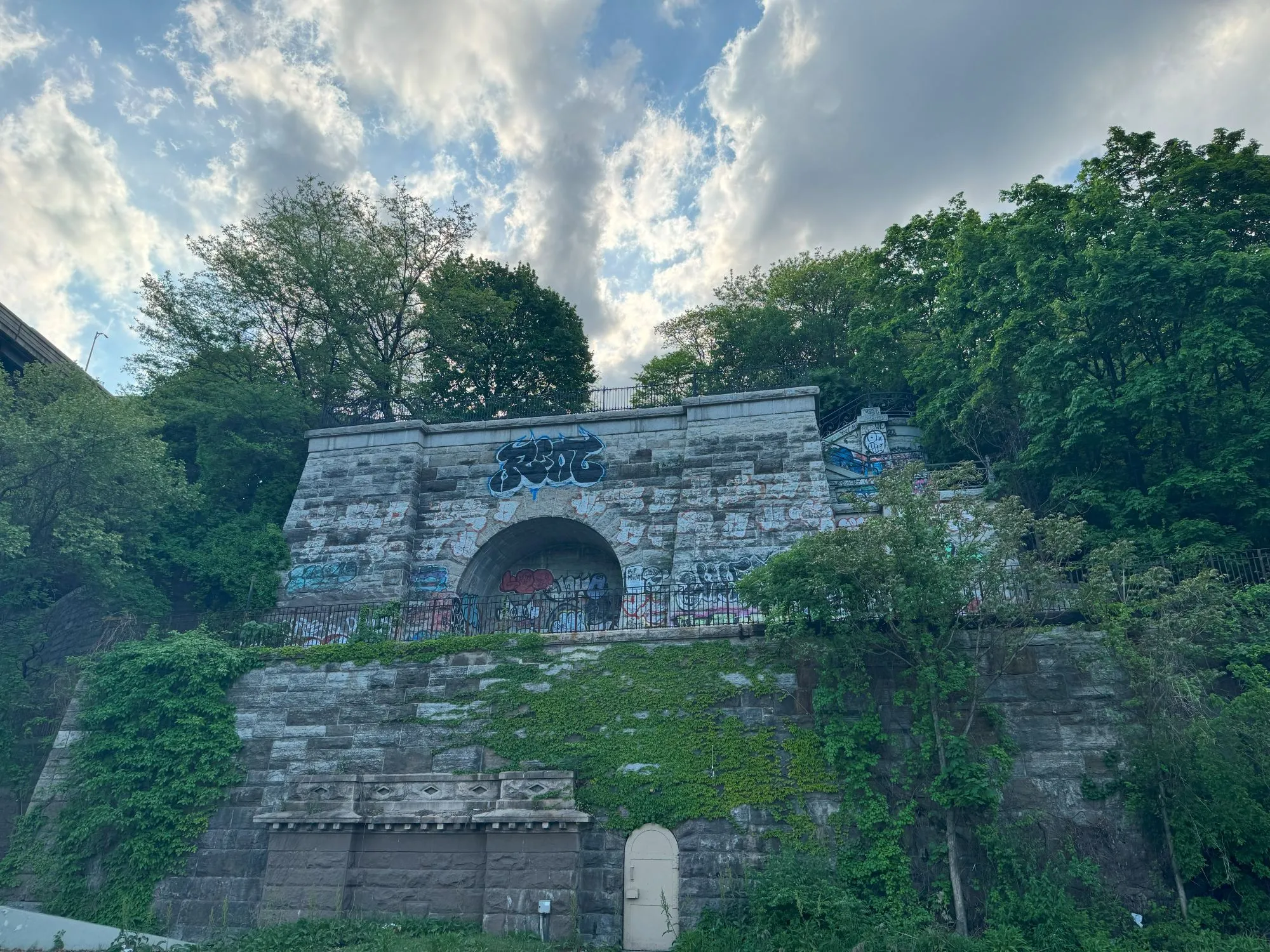 A stone structure overgrown with plants with assorted graffiti