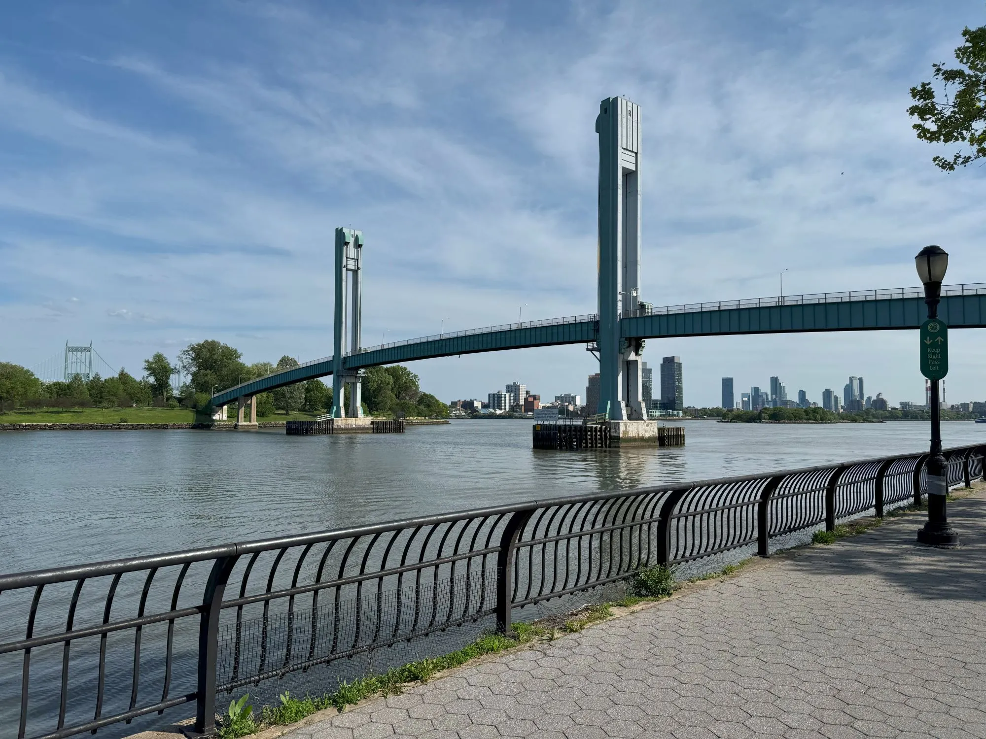A bridge going to a grassy area with tall buildings visible in the further distance