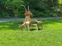 A strange wooden figure setting on a bench in a grassy field