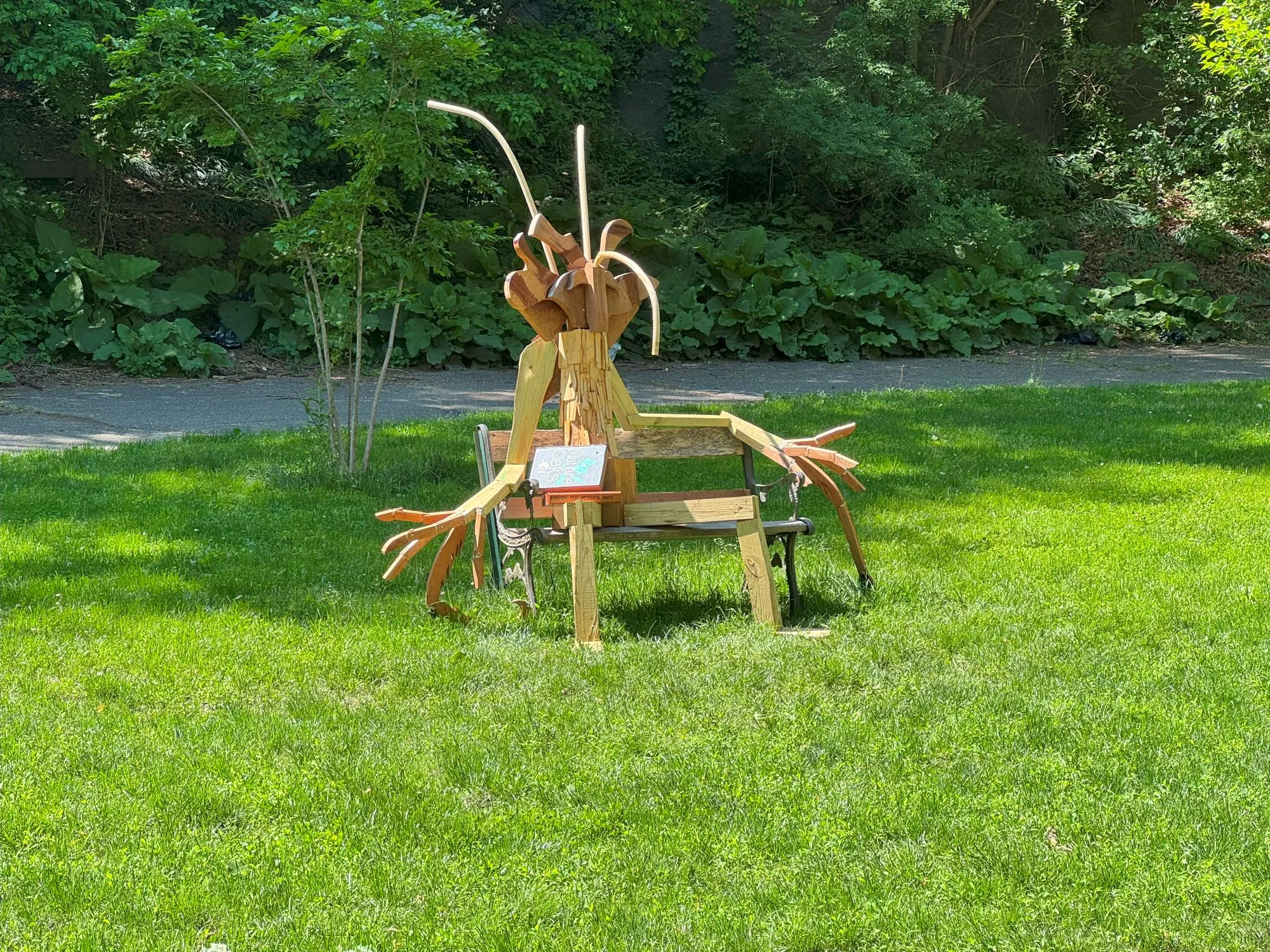 A strange wooden figure setting on a bench in a grassy field