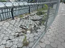 A broken section of path along the river, behind a chain-link fence