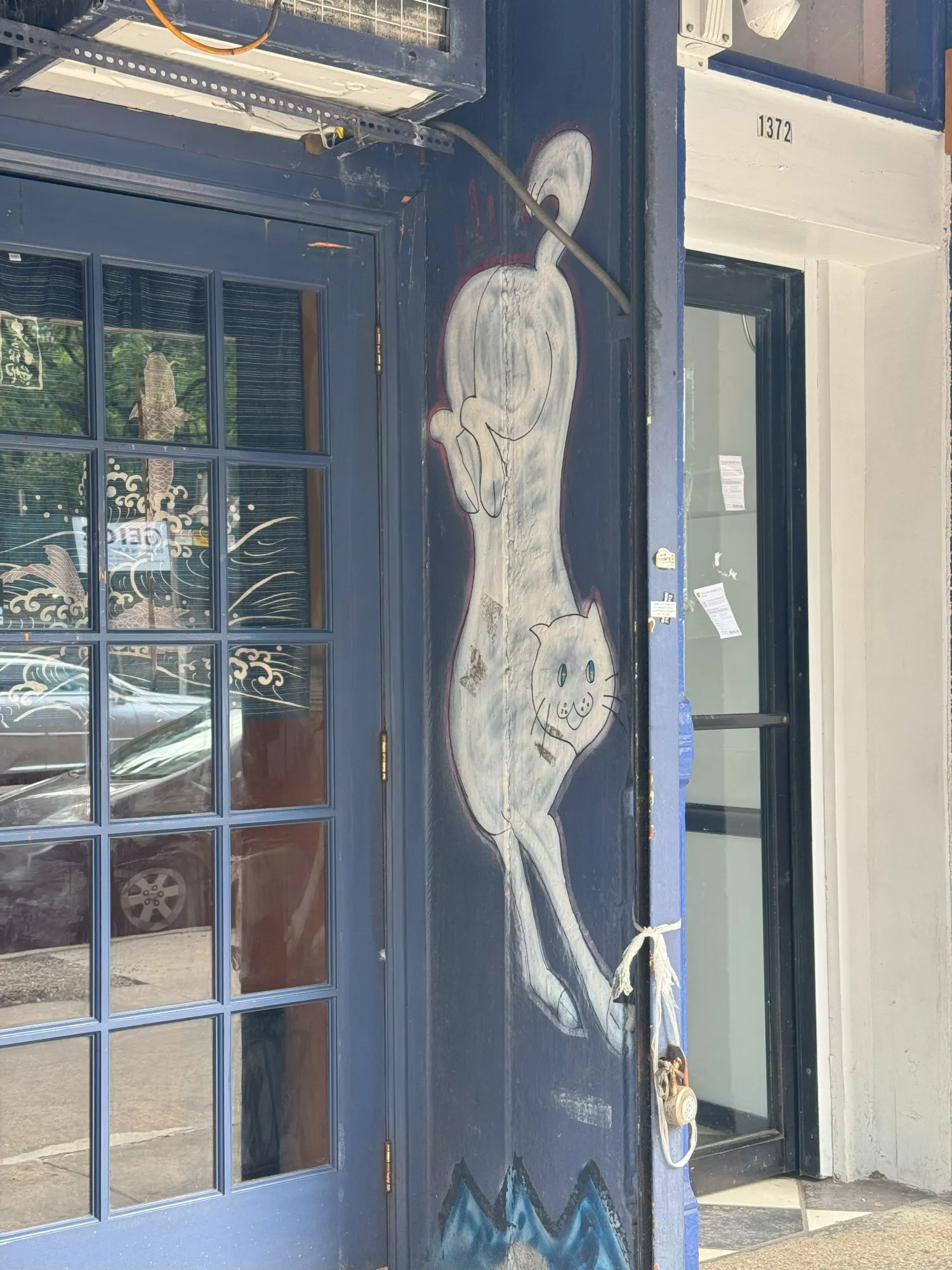 A white cat painted vertically on a purple background next to a door