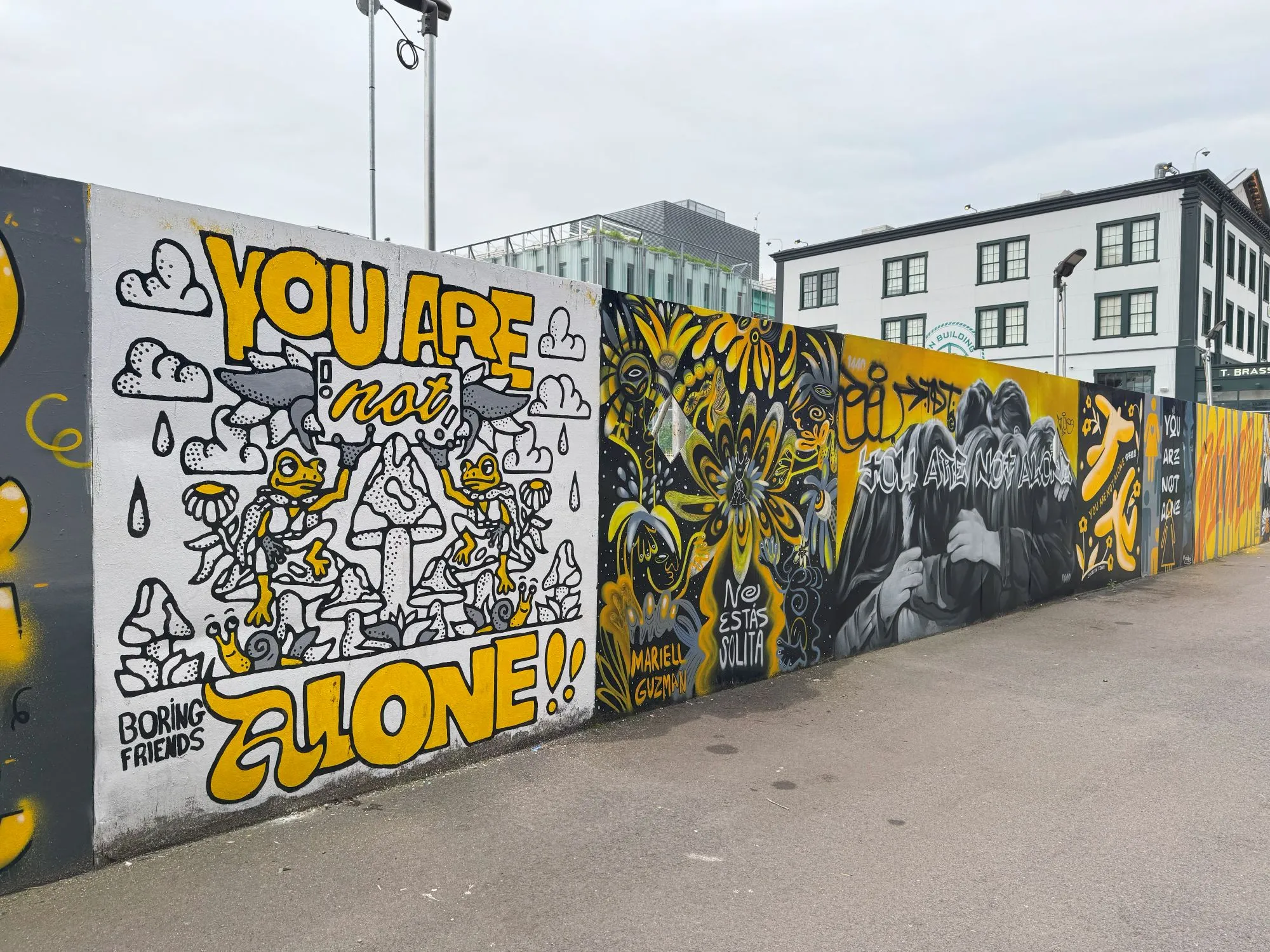 A series of murals in black, white, gray, and yellow, with the words 'You are not alone' on each