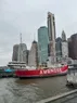A boat painted red with the name 'Ambrose', with many tall buildings in the background