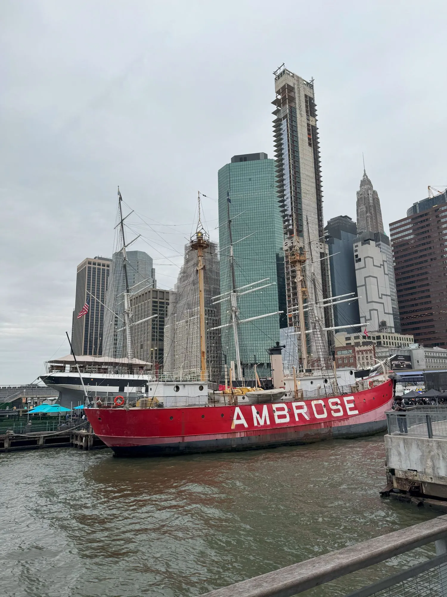 A boat painted red with the name 'Ambrose', with many tall buildings in the background