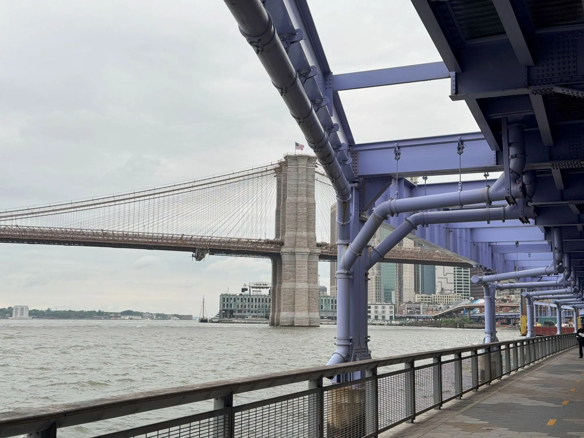 The Brooklyn Bridge in the distance from a walkway beneath a highway painted purple