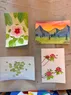 Four small watercolor paintings. One is of a mountainous landscape, one is of a flower, one is of flowers and a bee, and one is of lily pads